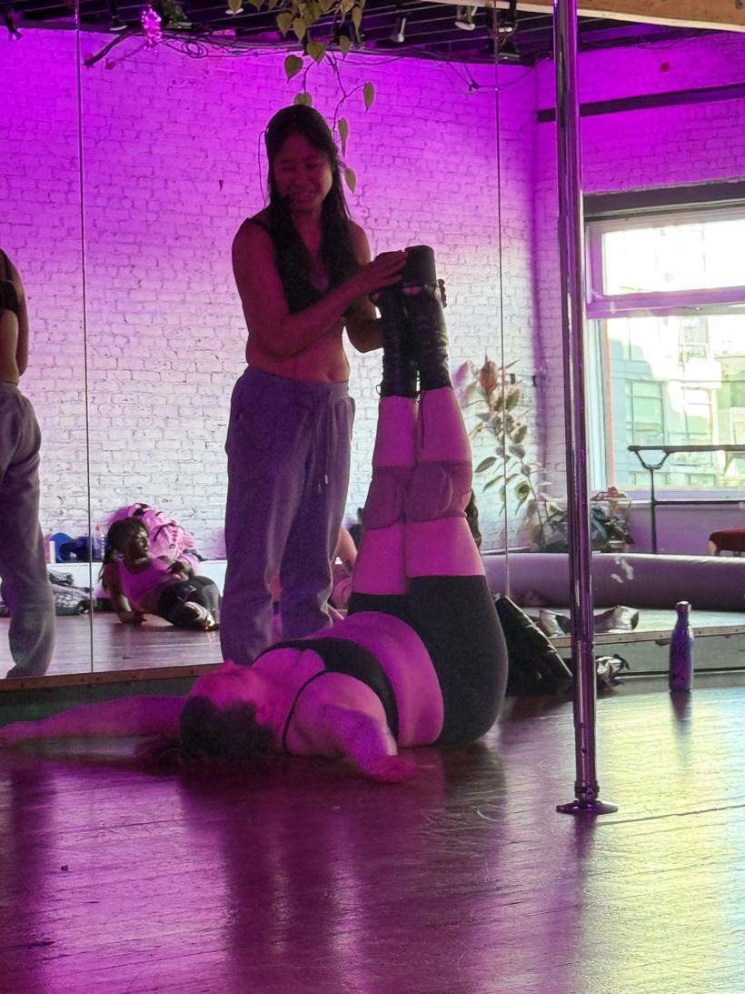 An instructor spotting a student through a shoulder stand in platform boots