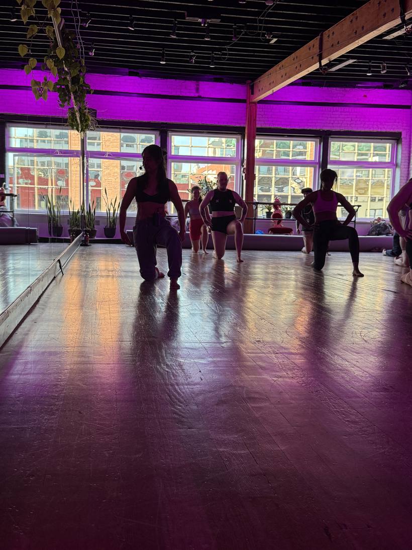 A group class warming up in a magenta-lit studio with tall windows